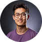 Smiling young man with glasses wearing a purple shirt against a dark gray background.