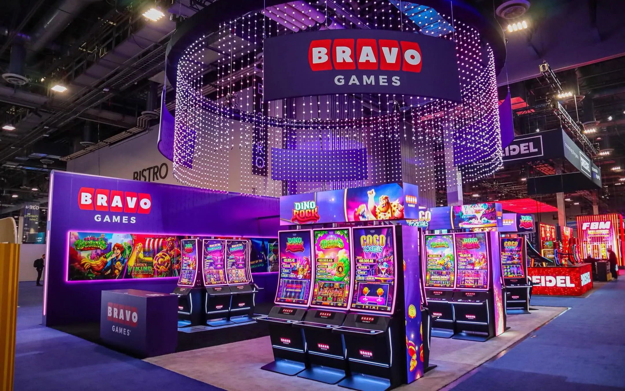 Stand da Bravo Games no G2E Las Vegas, com múltiplos gabinetes de slots, iluminação roxa e sinalização com logotipo da marca