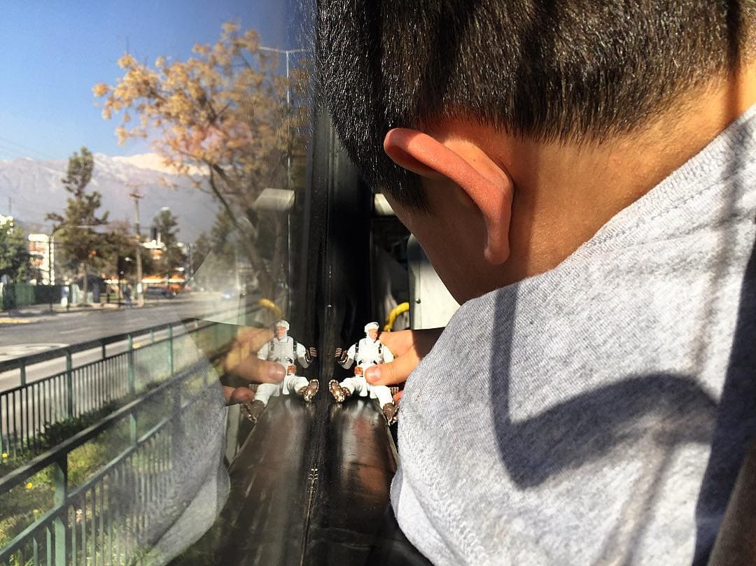 Un niño viajando en micro, mirando por la ventana y jugando con un juguete.