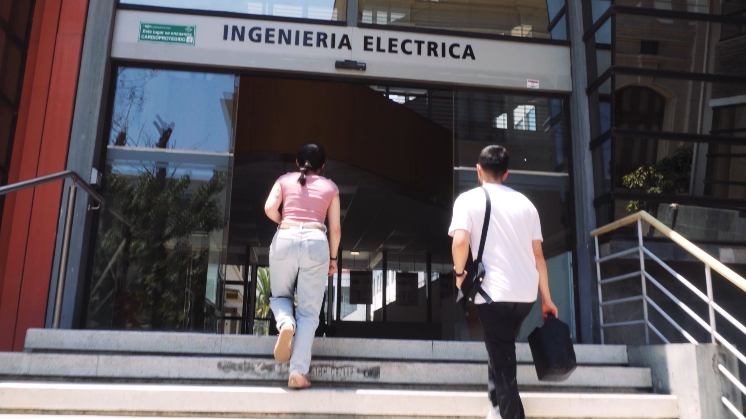 Dos estudiantes suben las escaleras hacia la entrada del edificio de Ingeniería Eléctrica de la Universidad de Chile.
