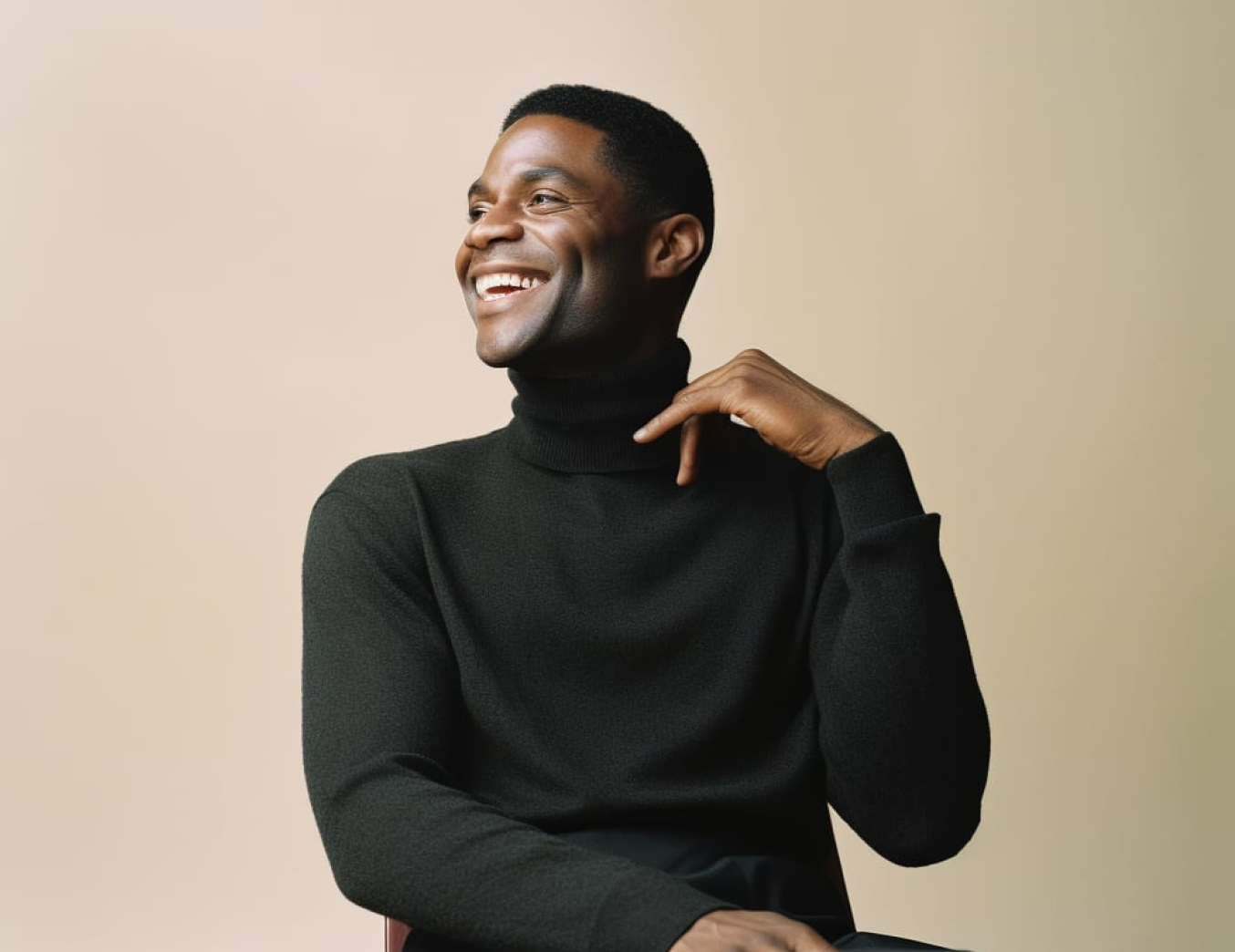 Smiling man wearing a black turtleneck sweater against a neutral beige background.