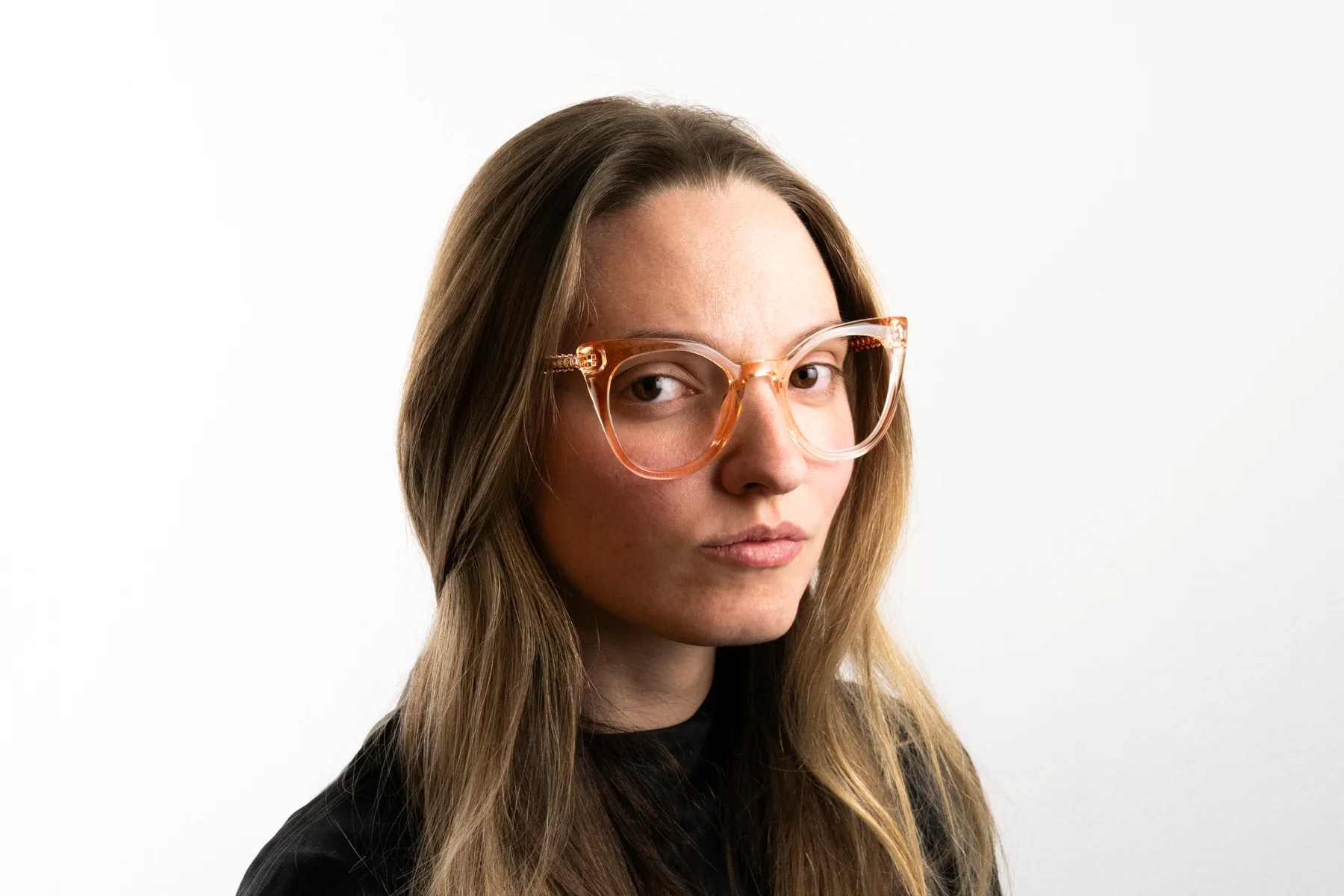 Donna con occhiali trasparenti arancioni e capelli lunghi castani contro sfondo bianco.