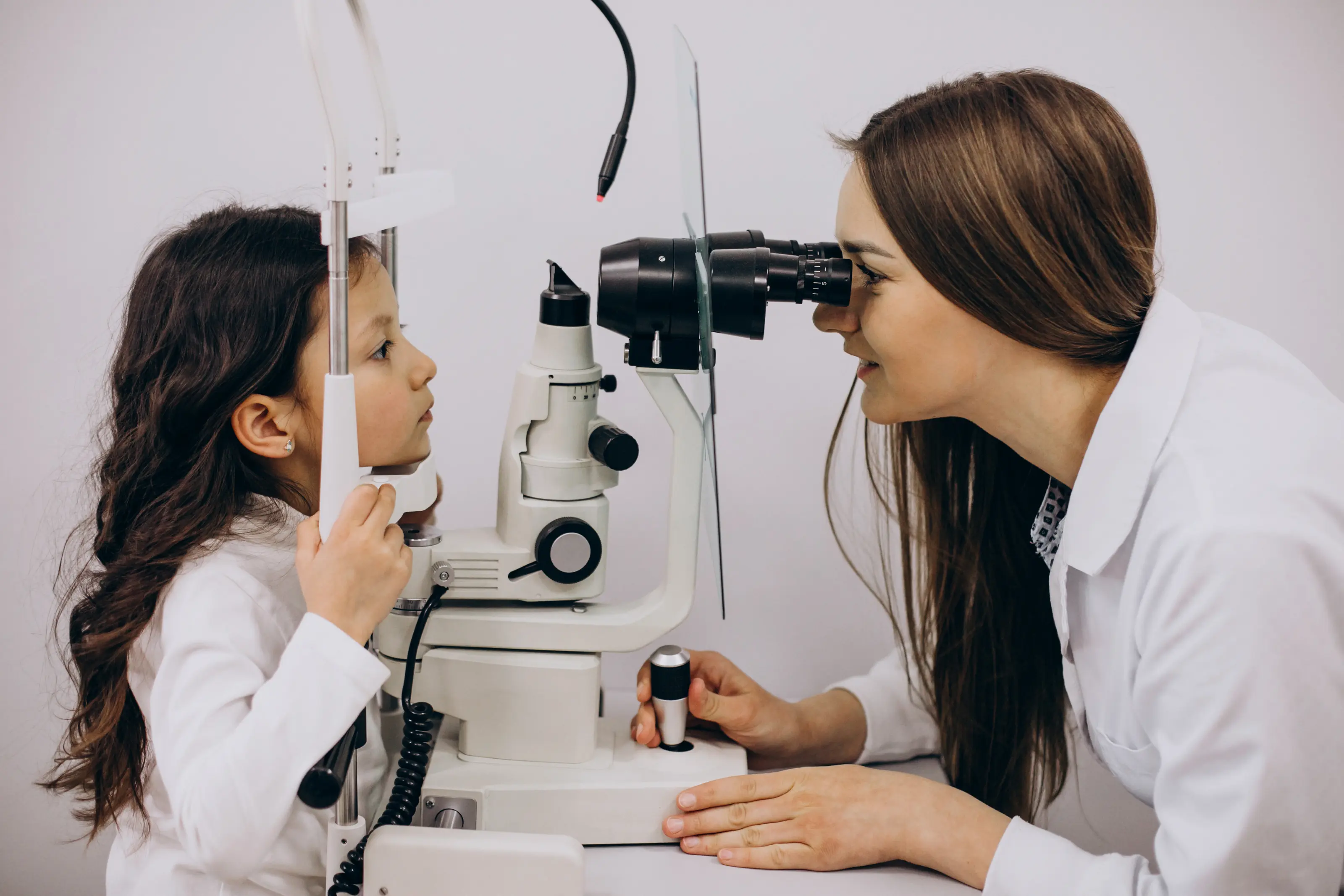 Una bambina fa un esame della vista con un'oftalmologa che usa uno slit lamp.