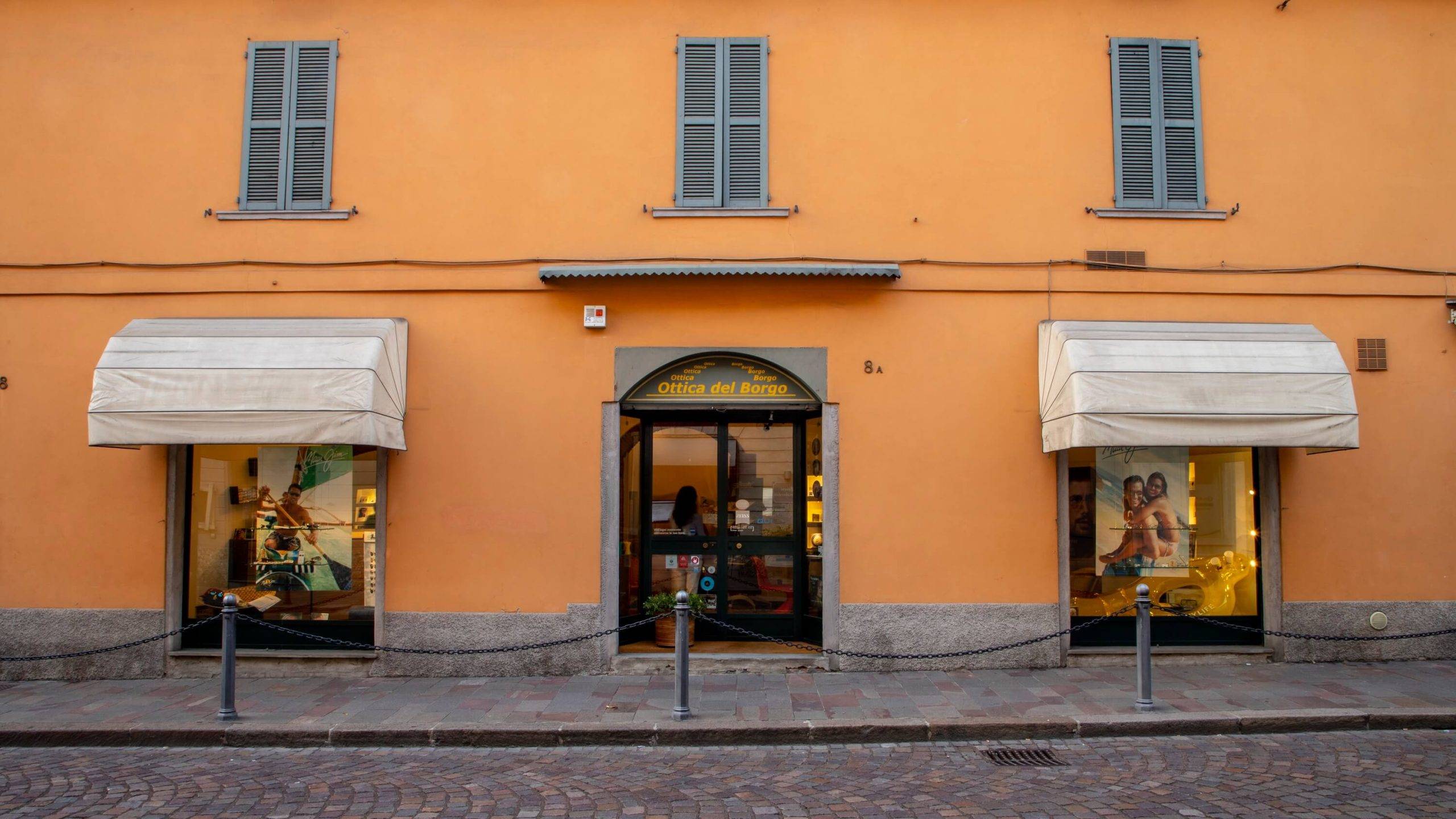 Facciata arancione di un negozio di ottica con due finestre e porta centrale con insegna Ottica del Borgo.