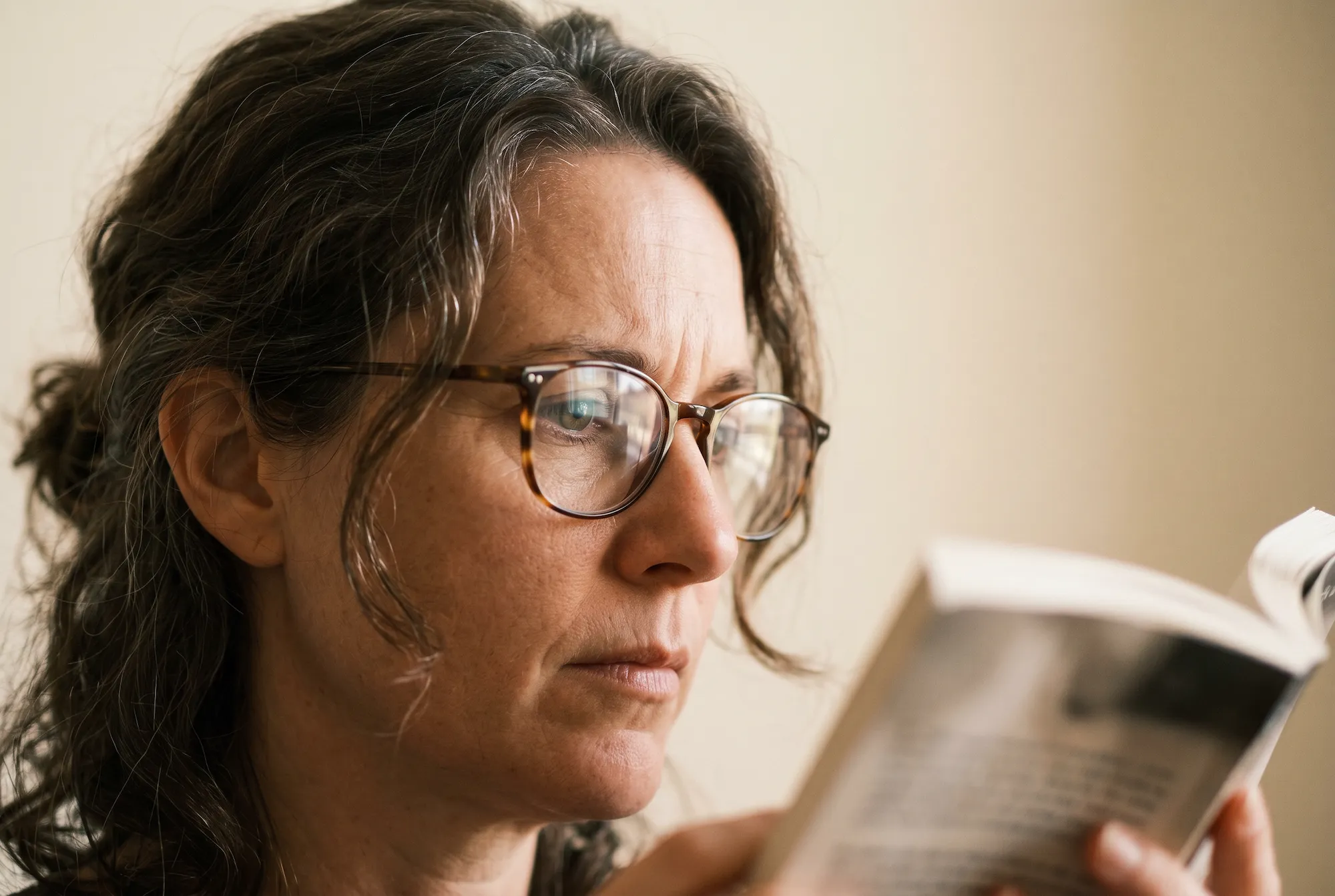 Donna con occhiali che legge attentamente un libro in primo piano.