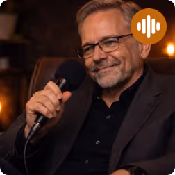 Mann mit Brille hält Mikrofon in einer gemütlichen, abgedunkelten Studioumgebung.