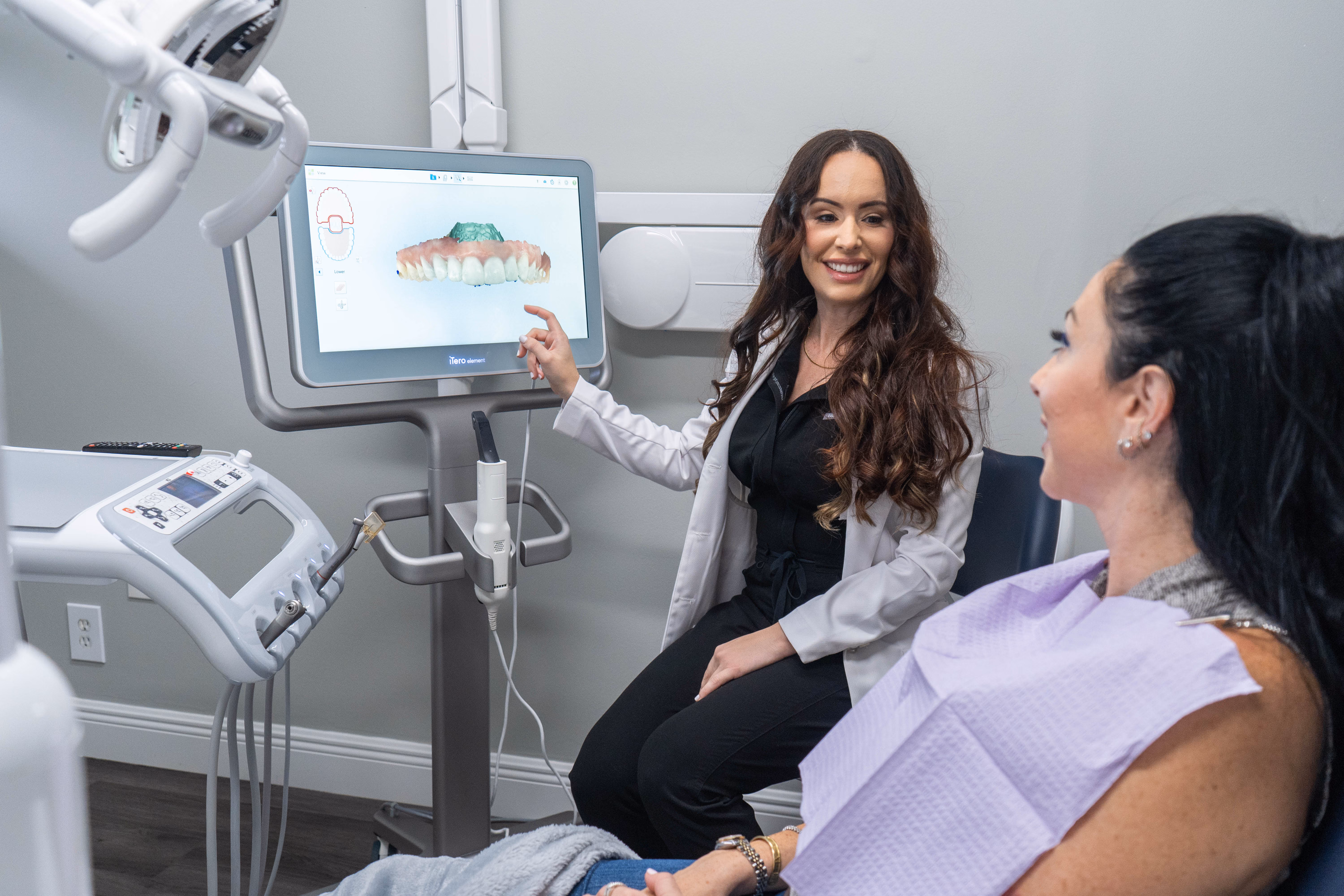 Dentist showing digital 3D dental scan on screen to female patient in dental office.