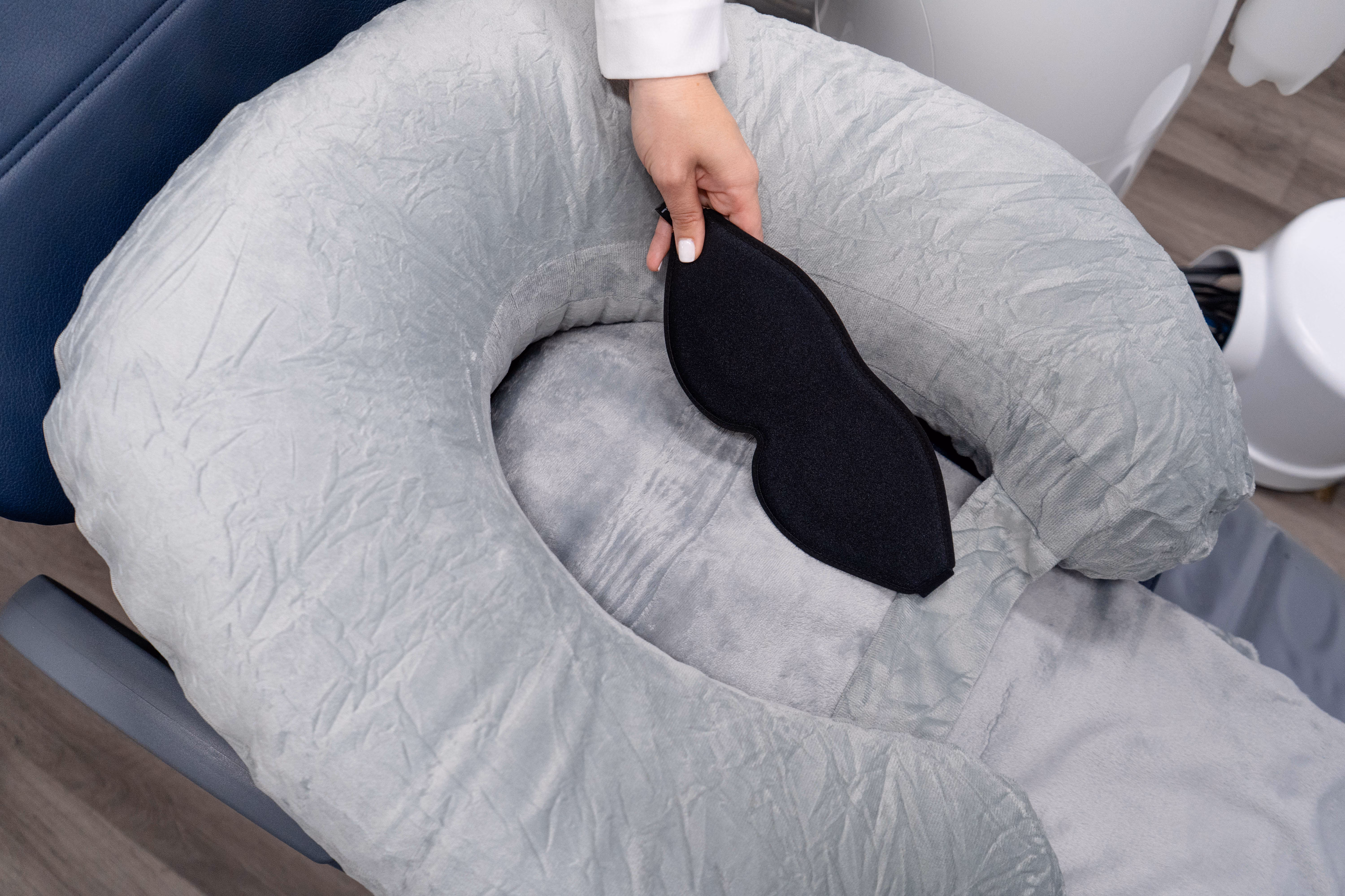 Hand placing a black eye mask on a gray padded headrest of a medical or spa chair.