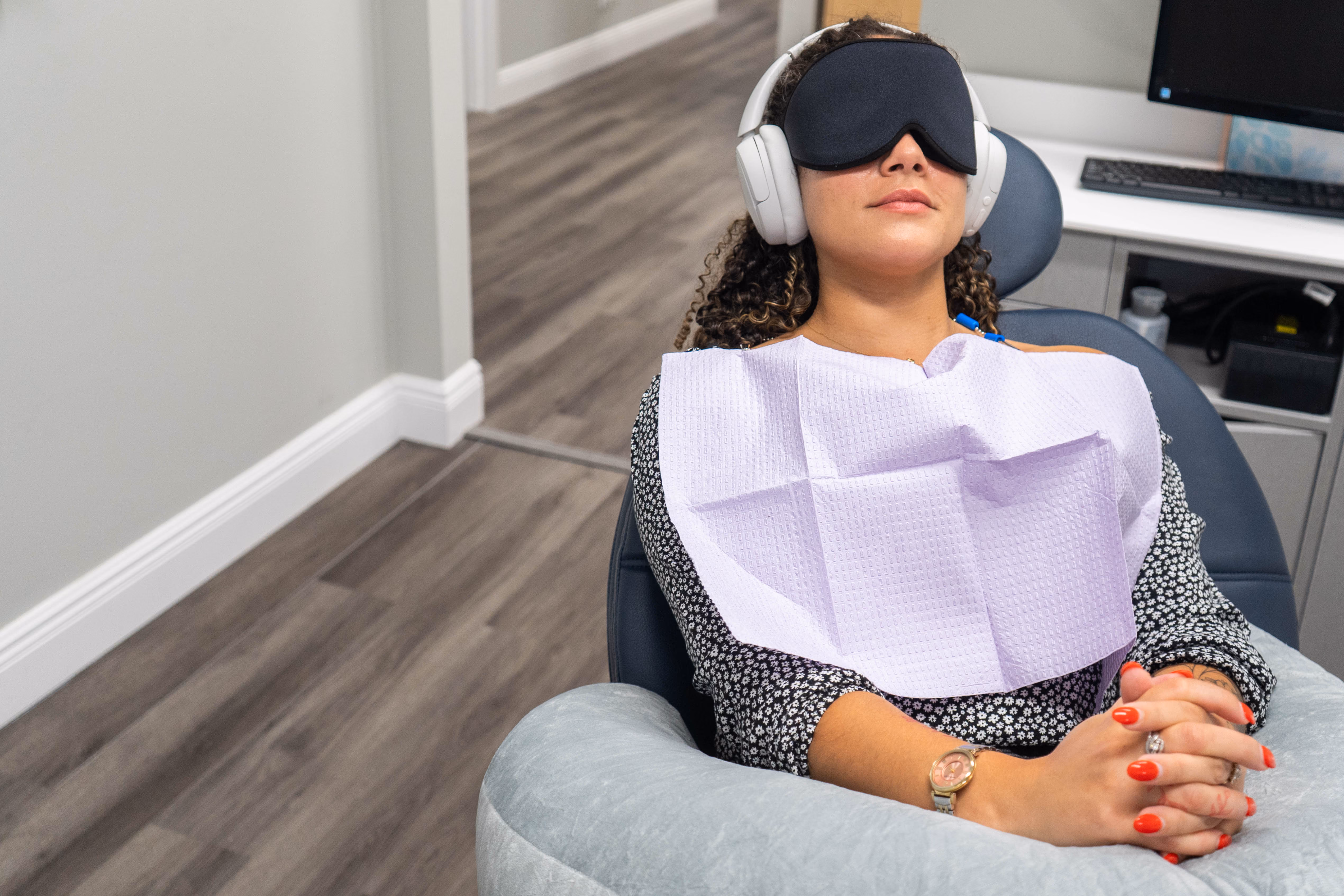 Woman reclining in dental chair wearing headphones and eye mask with a dental bib on.