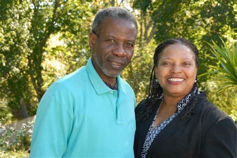Smiling middle-aged Black couple posing outdoors with trees in the background.