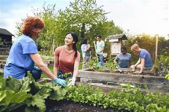 Two women smiling and working together in a raised garden bed with plants growing around them in a community garden.