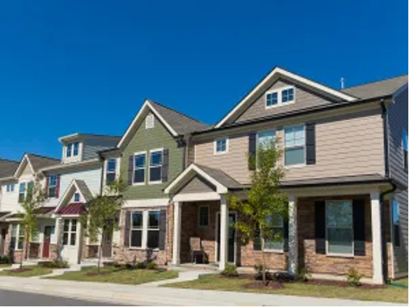 Row of modern suburban houses with porches and manicured lawns under a clear blue sky.