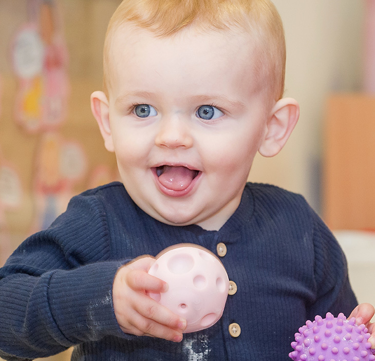 Smiling happy baby, playing with a plastic ball