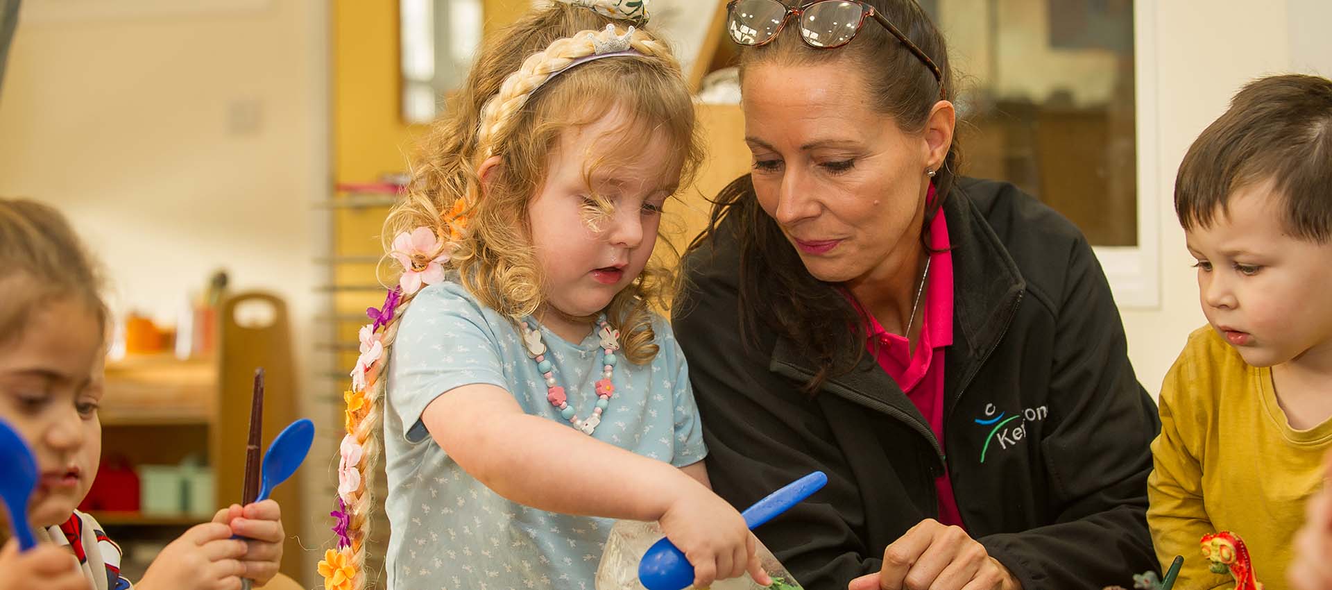 Teacher sitting with nursery children engaging with a little girl