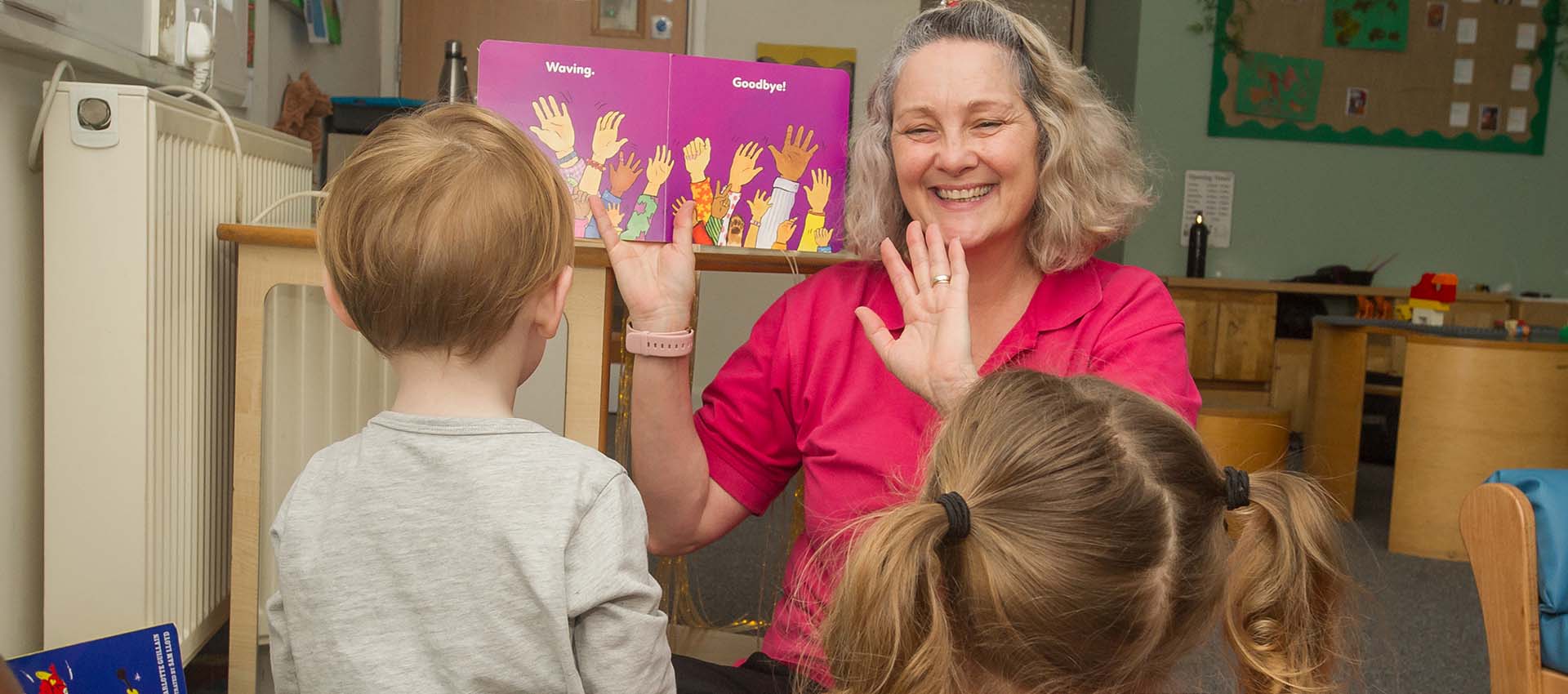 Teacher holding up a book about hands to her nursery class