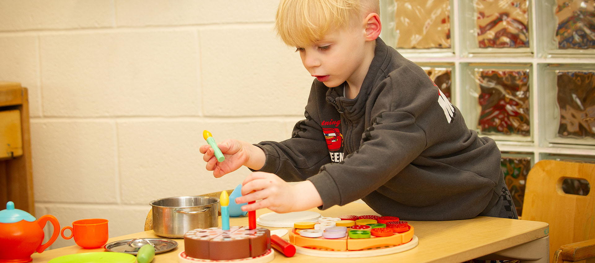 Boy placing plastic candles in a pretend cake at Keystone Nursery