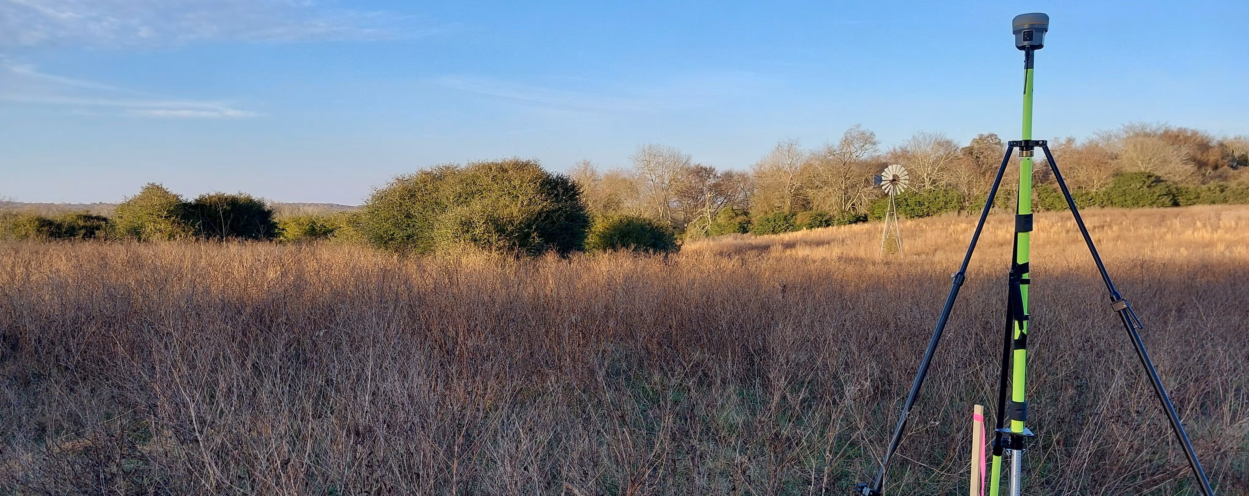 Trimble R10 GNSS receiver collecting raw static data over a known survey control point in an open field for aerial mapping.