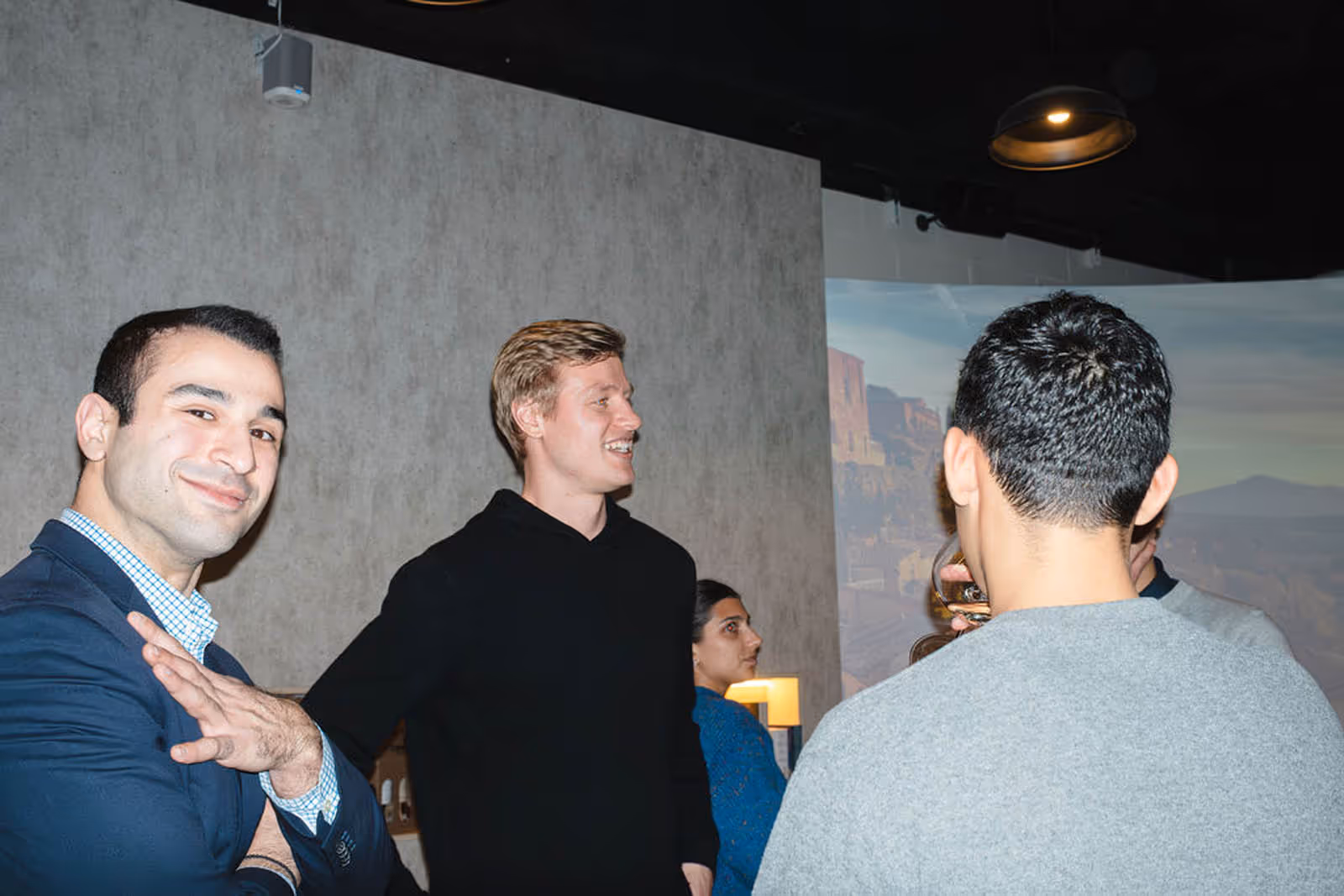 Group of four people socializing indoors, with one man in a suit smiling at the camera.
