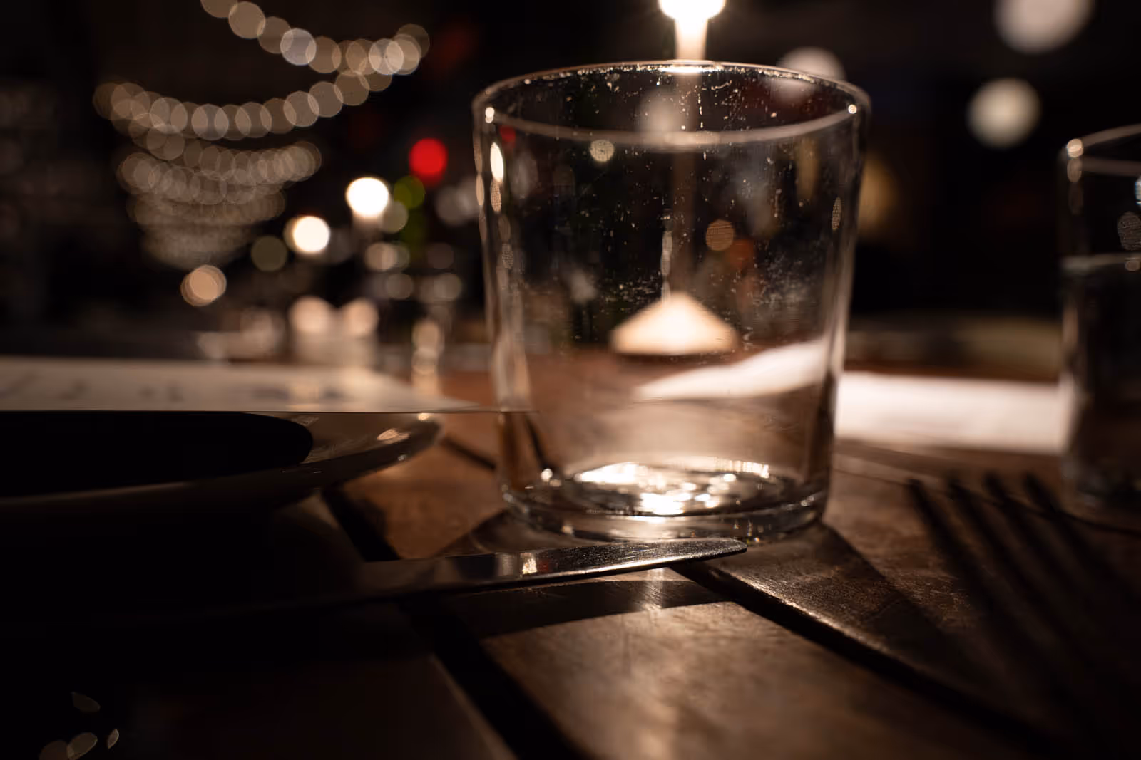 Empty clear drinking glass on a wooden table with blurred warm ambient lights in the background.
