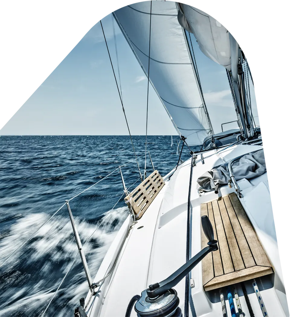 View from the deck of a sailboat sailing out to sea with white sails hoisted in the wind.