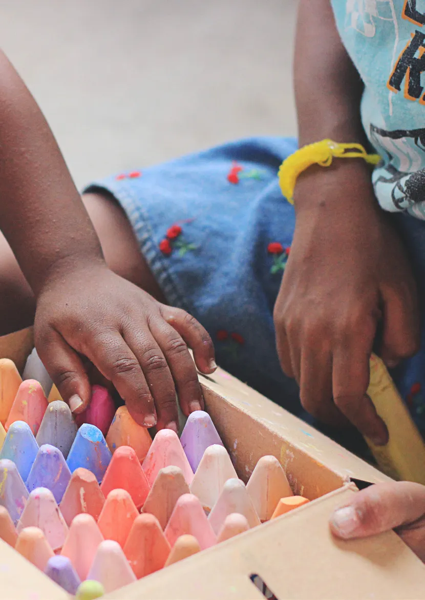 Child's hands holding and choosing colored crayons inside a cardboard box.
