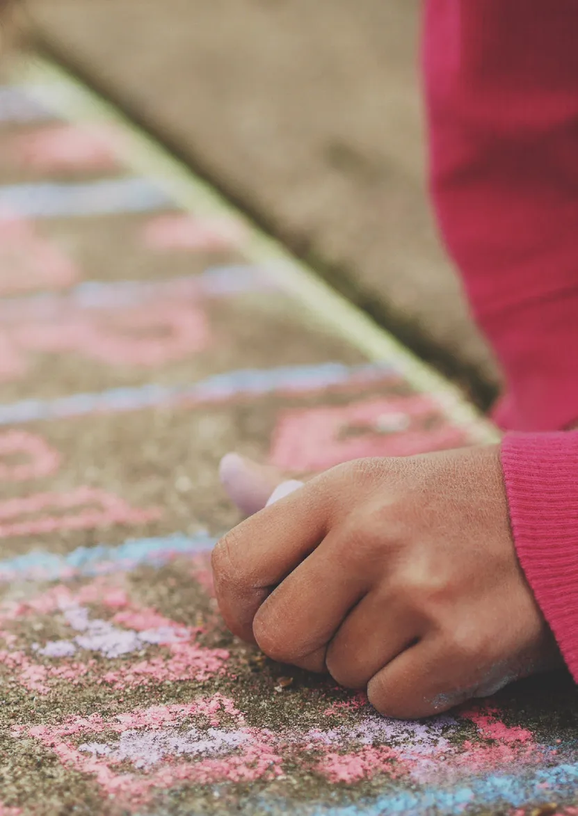 Child's hand drawing with colored chalk on the concrete floor.