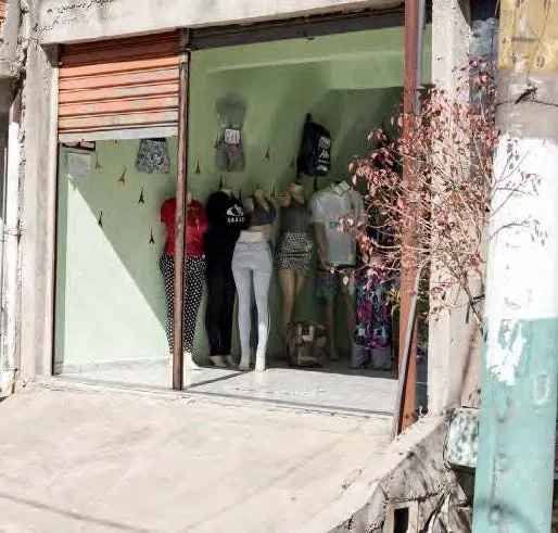 Vitrine de loja com cinco manequins vestidos com roupas femininas variadas, incluindo calças, shorts e blusas, em um espaço com parede verde e teto baixo.