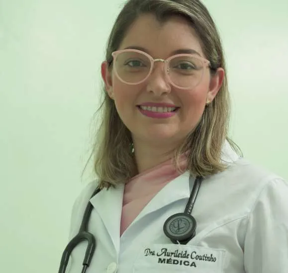 Doutora Aurileide Coutinho sorrindo, vestindo jaleco branco e estetoscópio.
