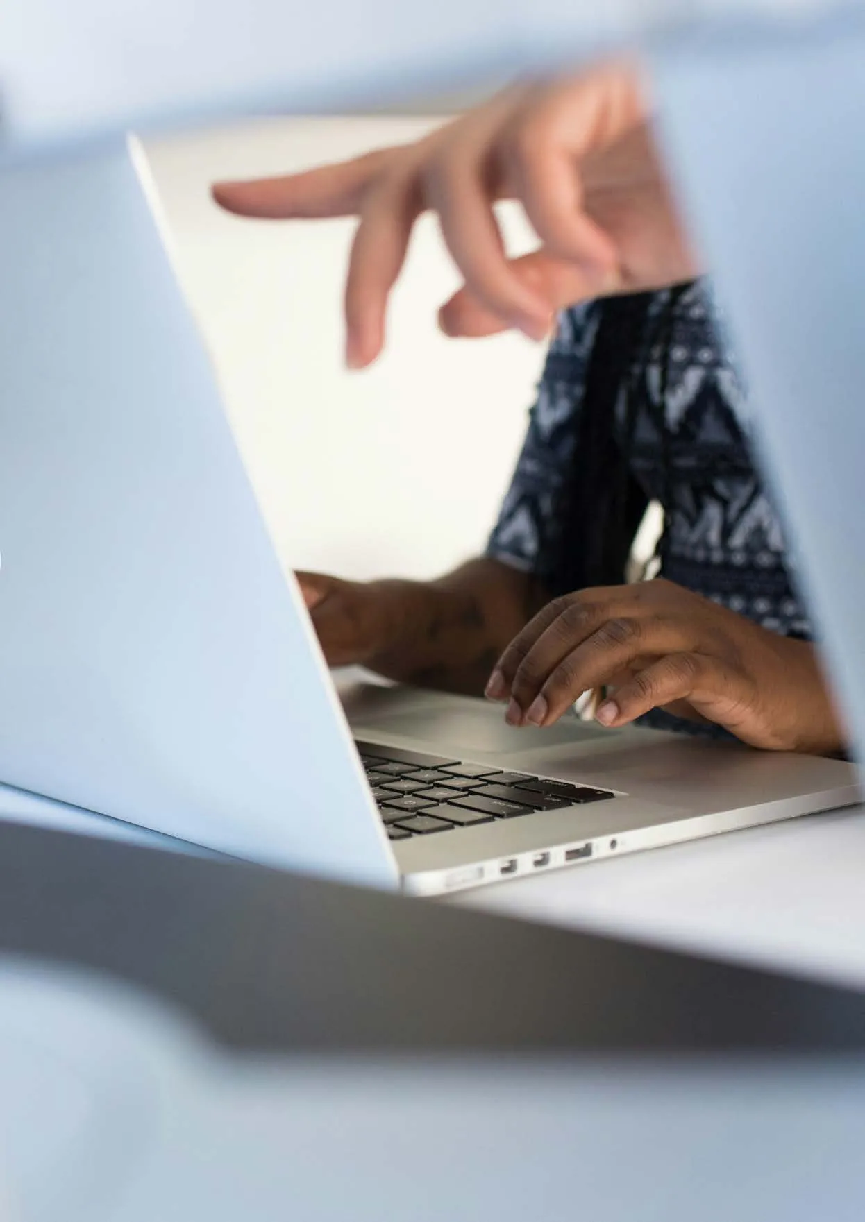 Mãos de uma pessoa digitando em um laptop prateado, com outra mão apontando na direção da tela.