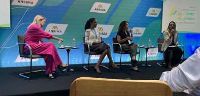 Quatro mulheres sentadas em cadeiras durante um painel de discussão em evento da ANBIMA.