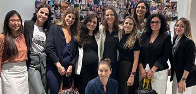 Grupo de dez mulheres posando juntas em um ambiente interno com uma parede decorada com várias fotos ao fundo.