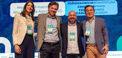 Quatro pessoas sorrindo, usando crachás em um evento com fundo azul e nomes em destaque.