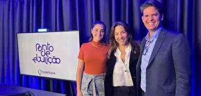 Três pessoas sorrindo em frente a uma tela que mostra o logo do podcast 'Ponto de Ebulição' e do Quintessa.