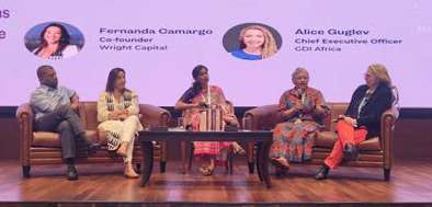 Cinco pessoas sentadas em um painel de discussão no palco, com projeção ao fundo mostrando fotos e nomes de Fernanda Camargo e Alice Guslby.