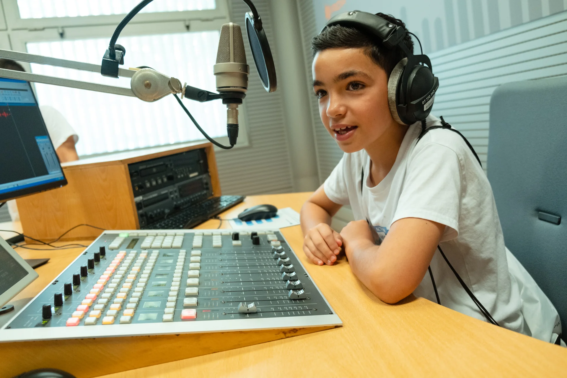 Rapaz com auscultadores fala para microfone em estúdio de rádio.