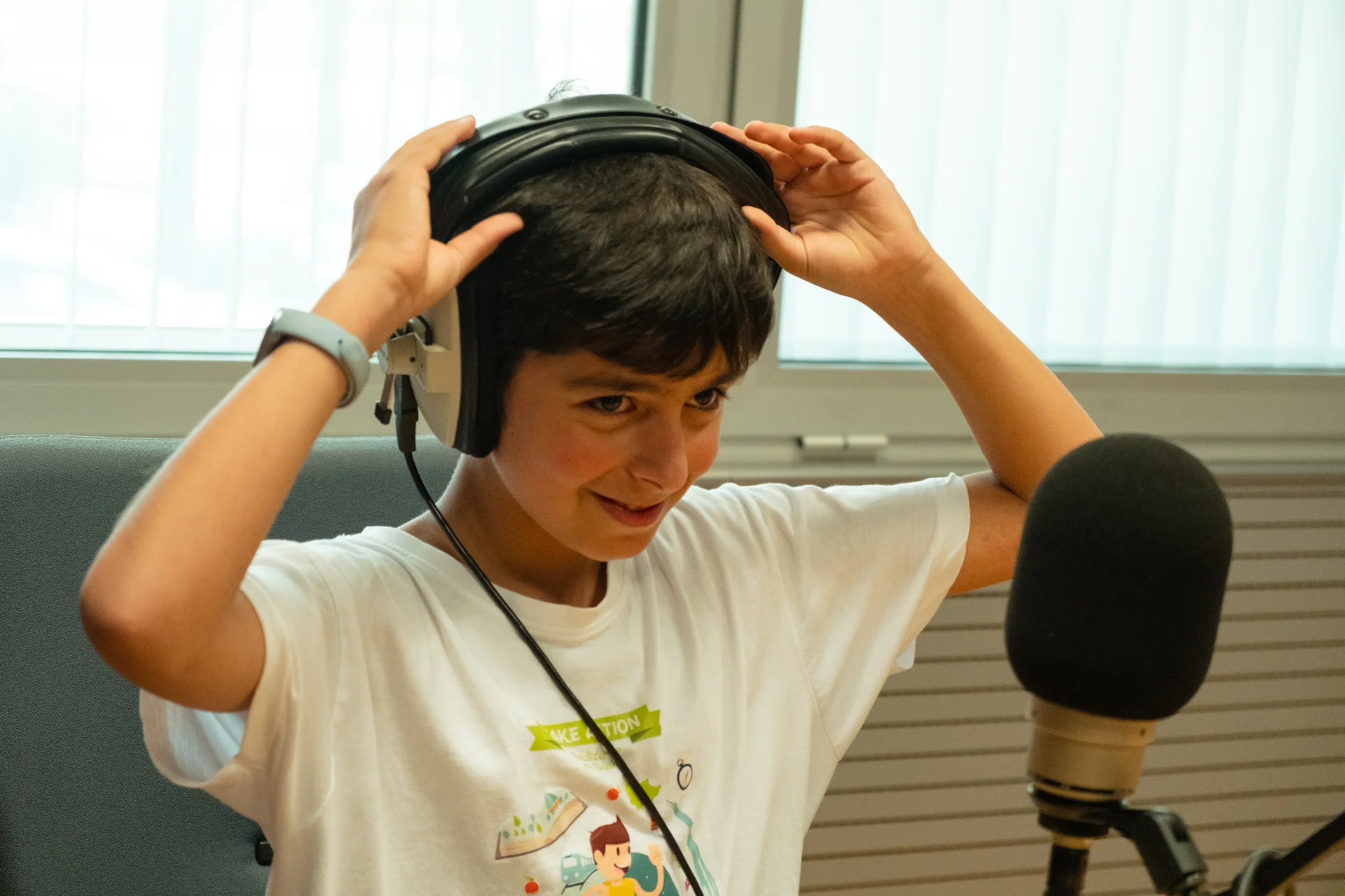 Rapaz a colocar auscultadores grandes numa sala com microfone de estúdio.