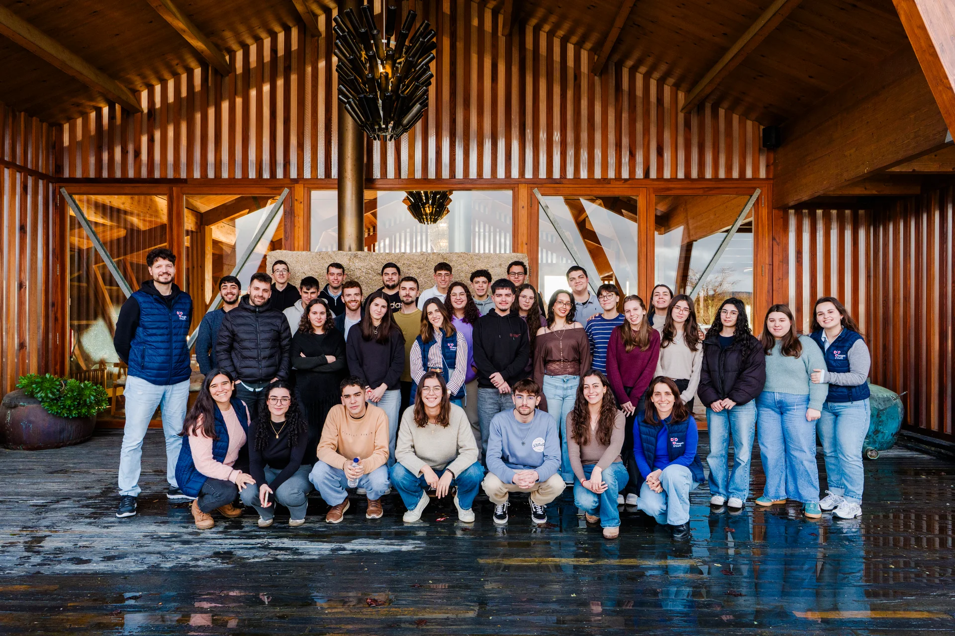 Grupo de jovens e docentes sorridentes em pose coletiva em frente a um edifício.