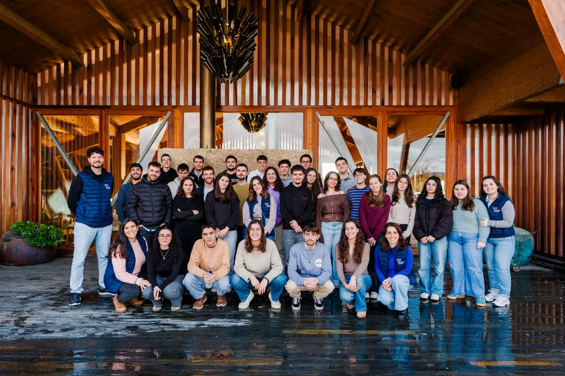 Grupo de jovens e docentes sorridentes em pose coletiva em frente a um edifício.