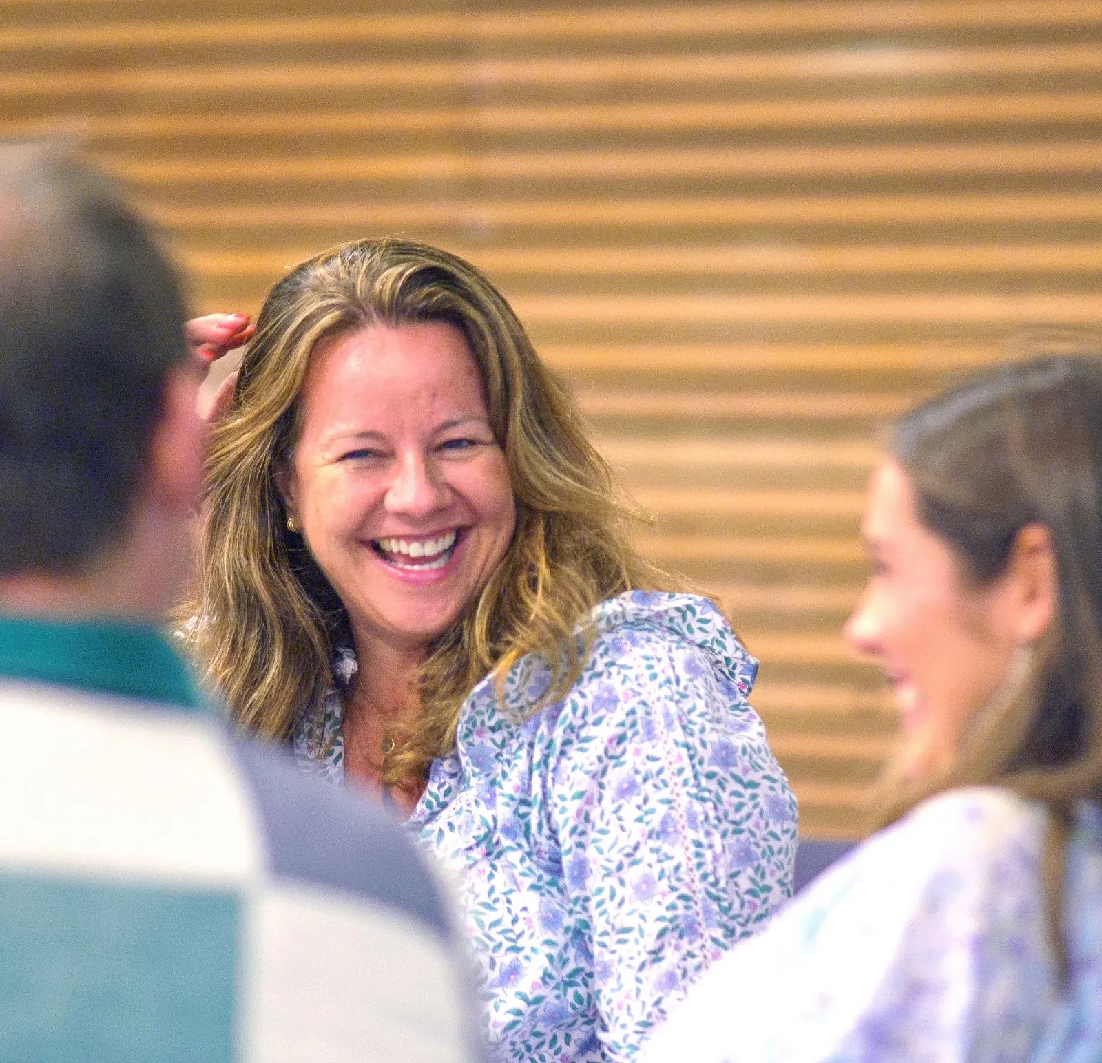 In a Thompson Harrison workshop, a participant, a woman with blonde hair wearing a floral blouse is laughing while talking to colleagues