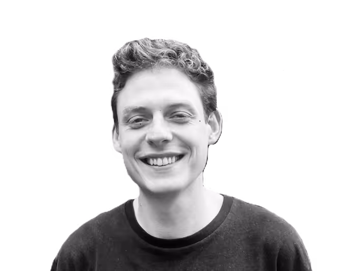 Jack B with curly hair wearing a dark shirt and smiling against a transparent background.