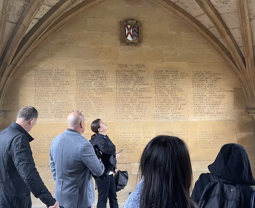 People observing names engraved on a large stone memorial wall under an arched ceiling on a team walk as part of a Thompson Harrison experience.