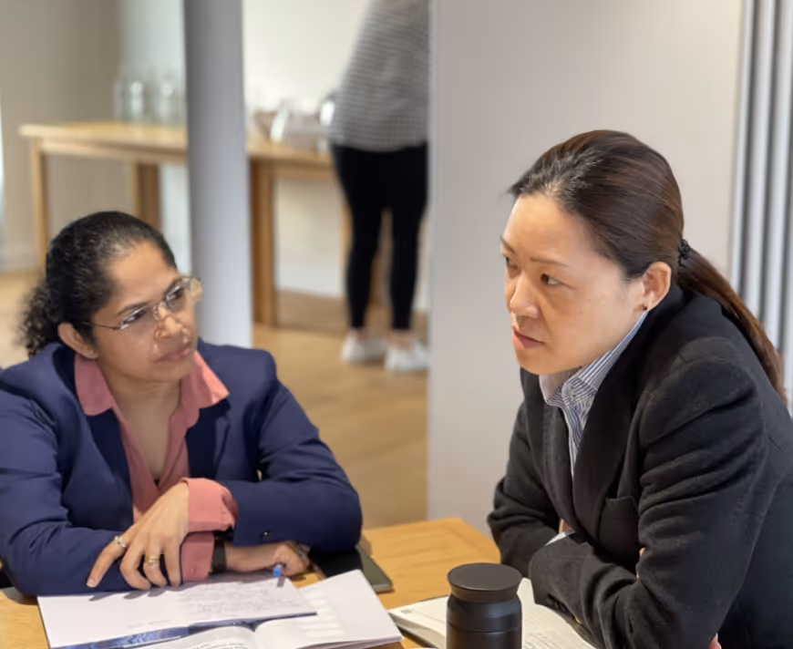 Two professional women engaged in a serious discussion over documents at a table.