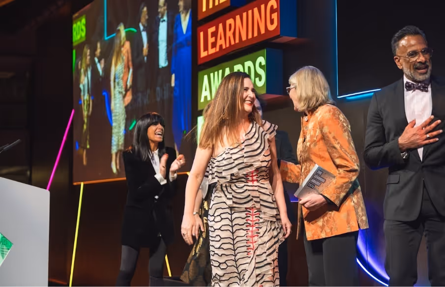 Thompson Harrison's Tracey, Sam and Gavin on stage smiling during an awards event with a large screen and 'Learning Awards' signage in the background.