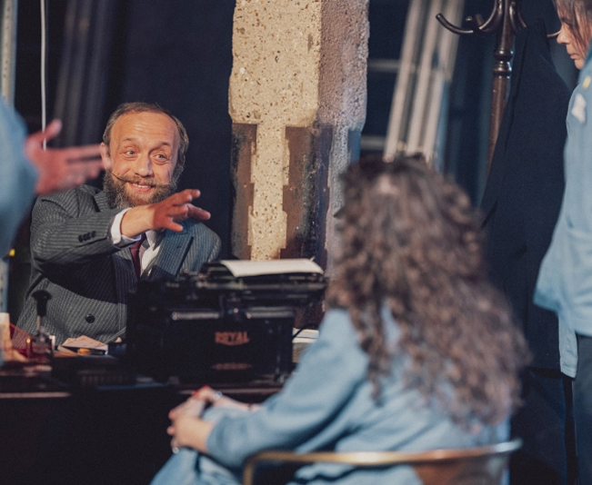 Bearded man smiling and reaching out at a desk with typewriter while woman with curly hair sits nearby as part of an organisational development session.