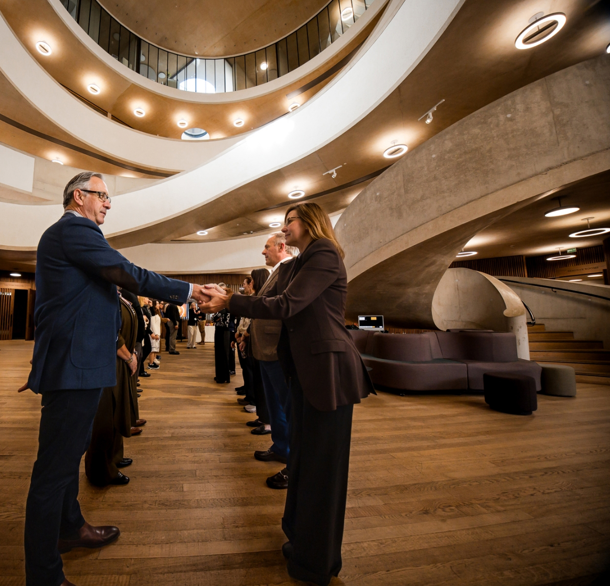 People shaking hands in a modern building with curved balconies and warm lighting.