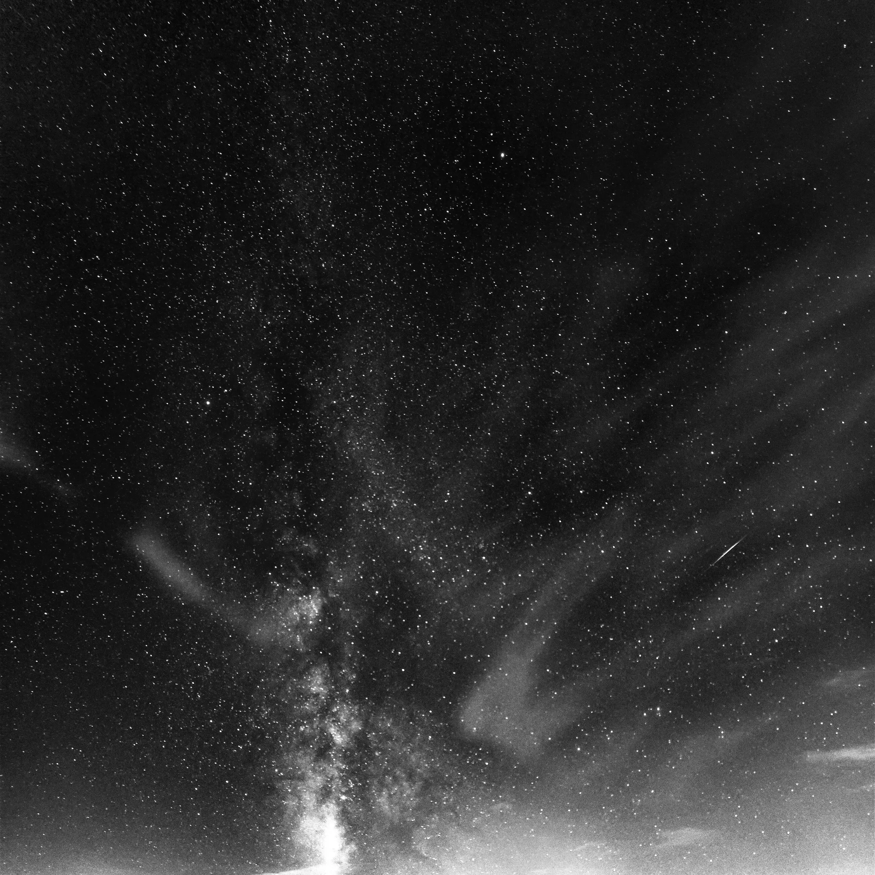 Starry night sky with the Milky Way and a bright shooting star above a glowing horizon.