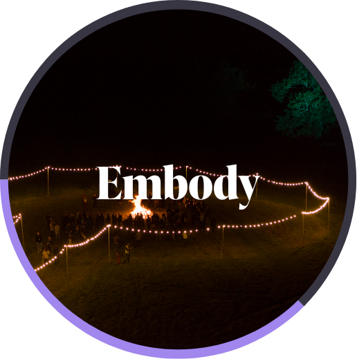 People gathered around a large campfire at night outlined by string lights forming a shape on grass.