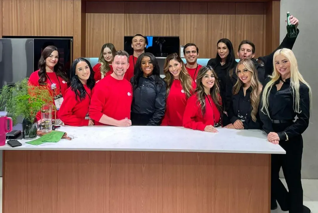 Booth team in red sweaters and black outfits gathered at a kitchen demo counter