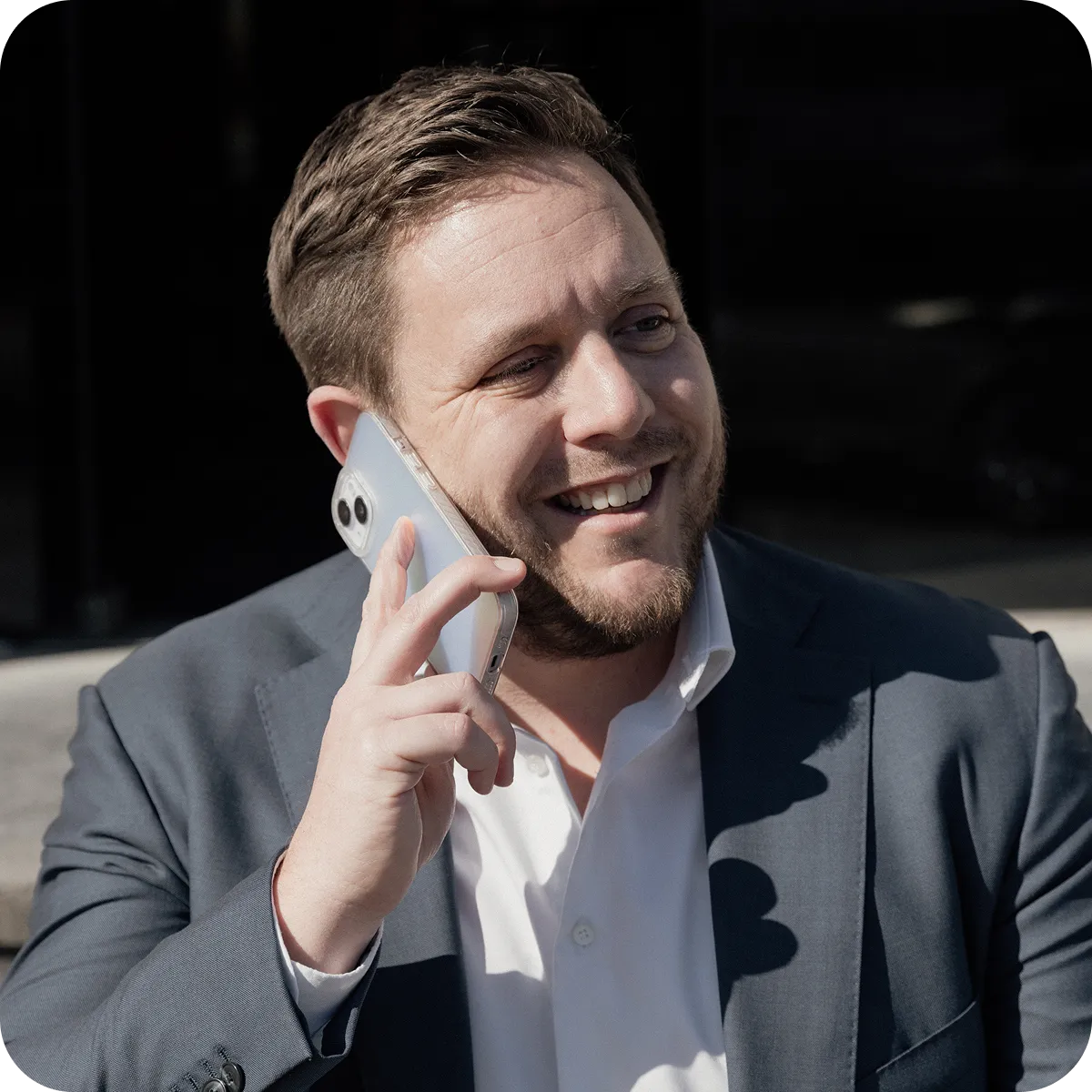Smiling man in a suit talking on a smartphone outdoors in daylight.