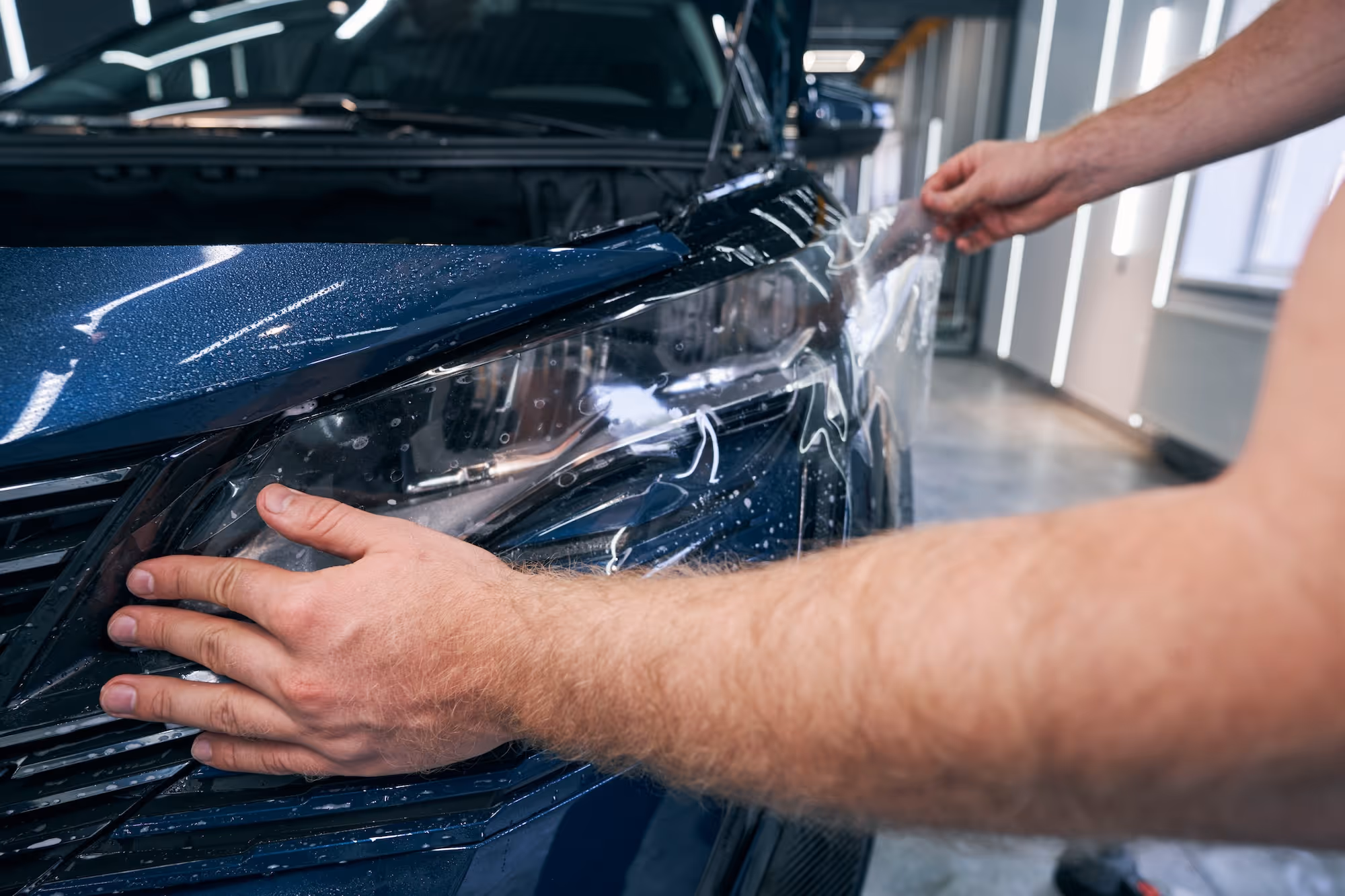 Collision repair professional applying film to the headlight of a car.